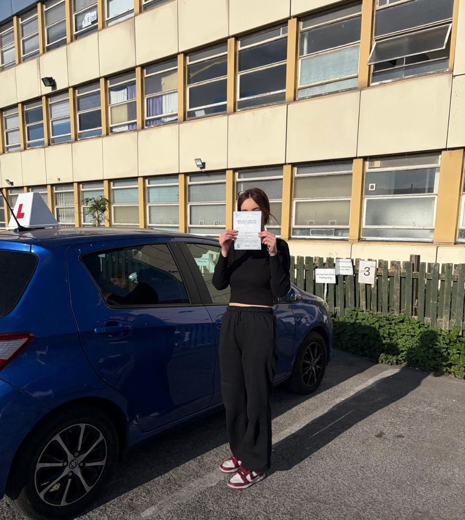 Passed student holding a driving test pass certificate beside a blue learner car