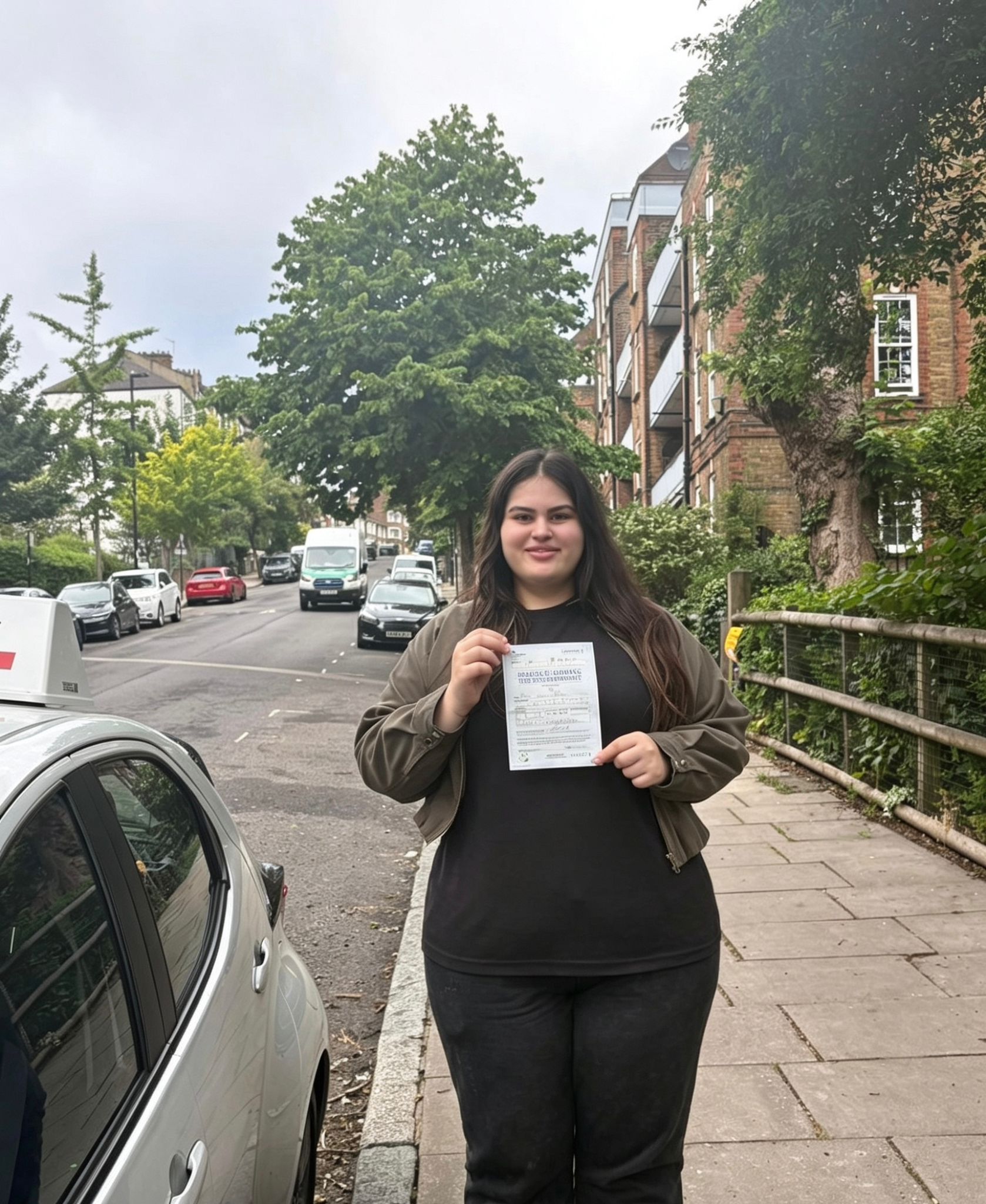 Passed student holding a driving test pass certificate on a North London street