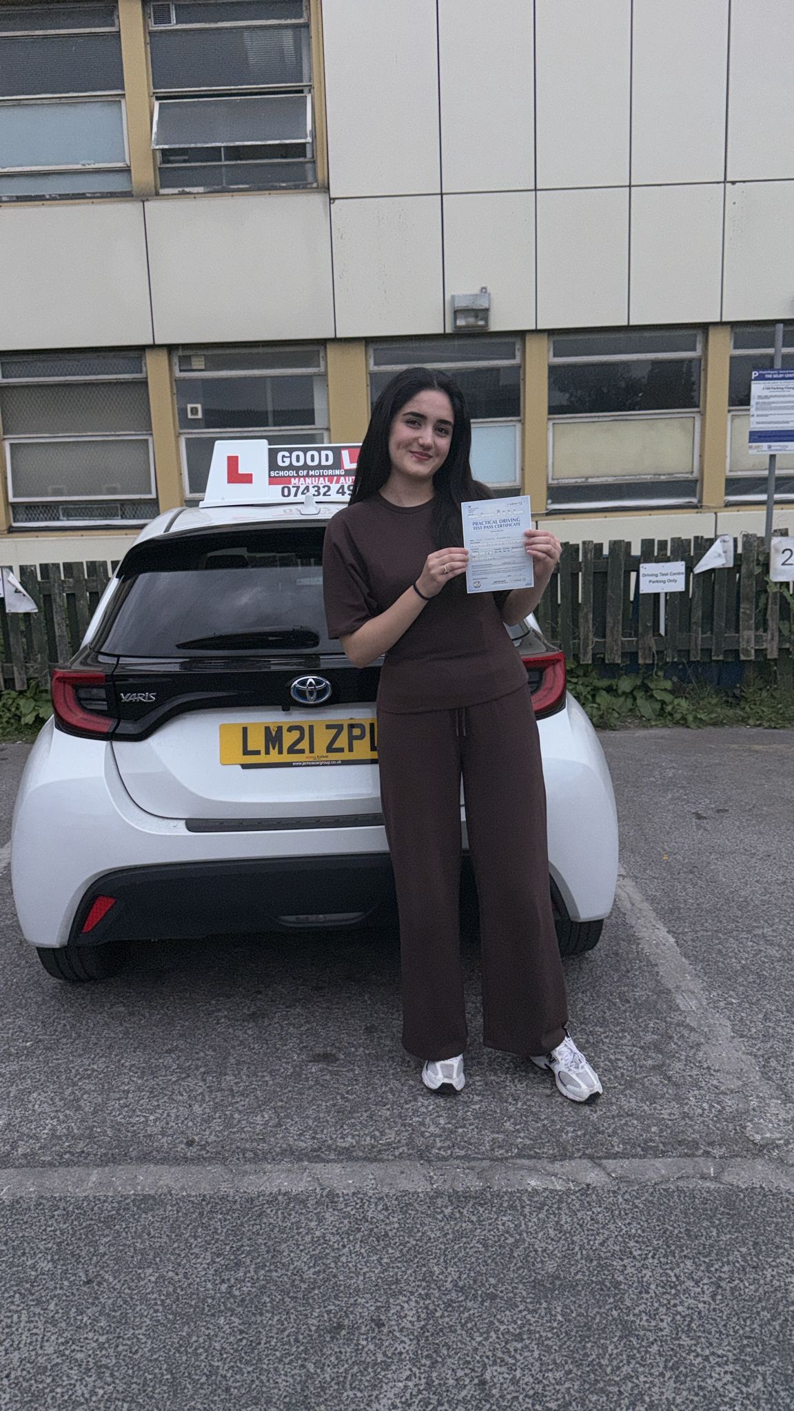 Passed student holding a driving test pass certificate beside a learner car