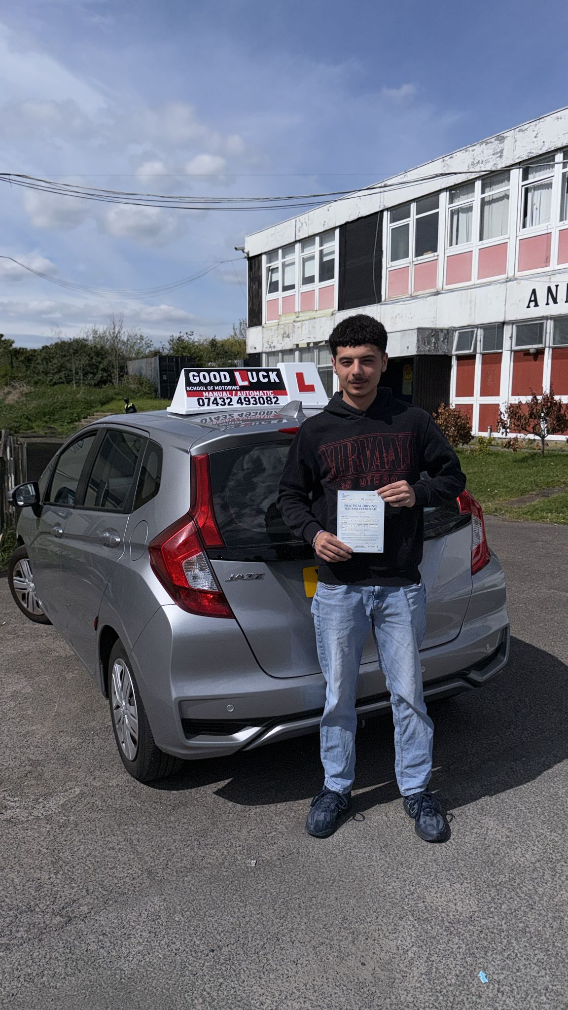 Passed student holding a driving test pass certificate beside a silver learner car