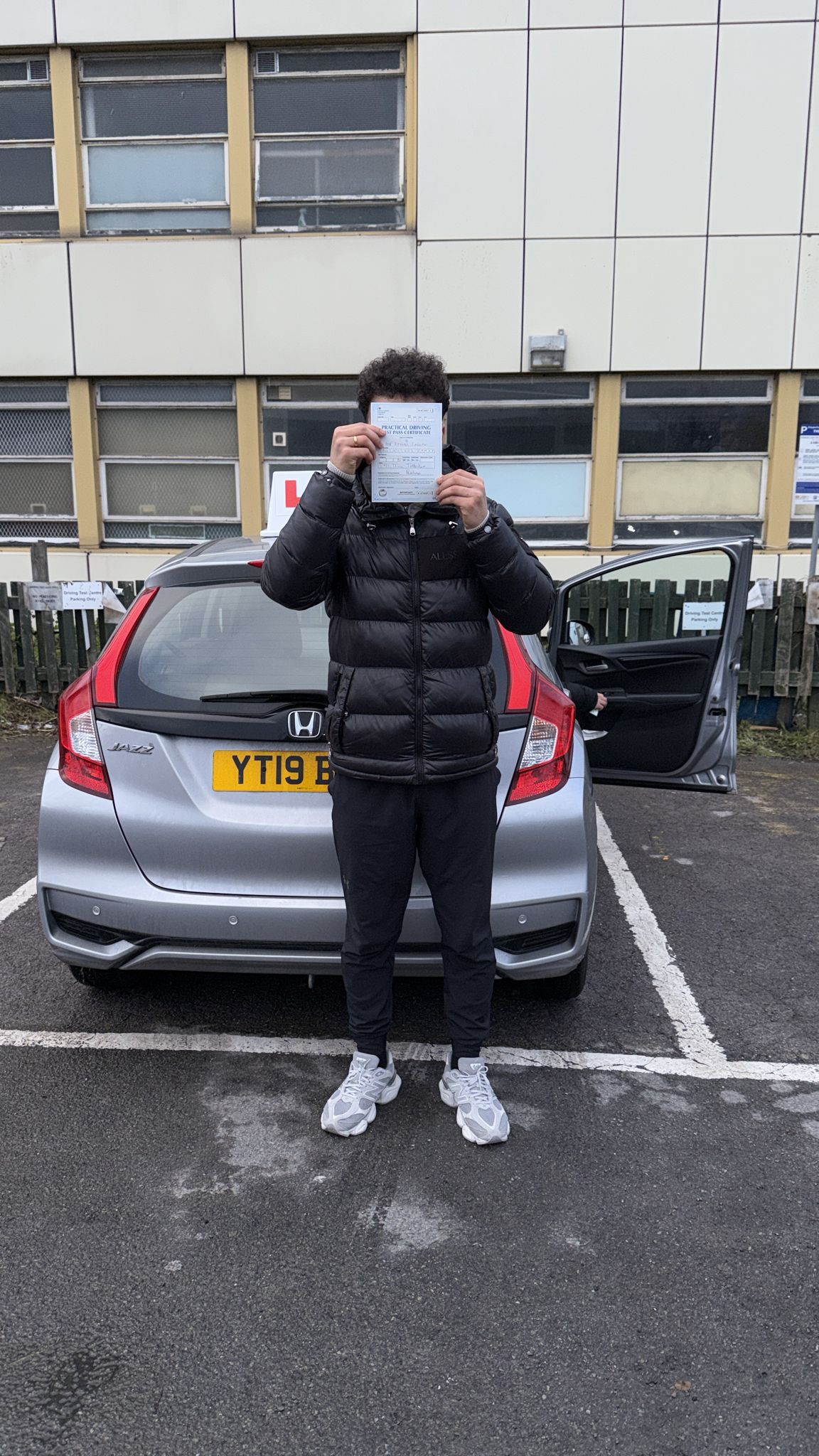 Passed student holding a driving test pass certificate in front of a learner car