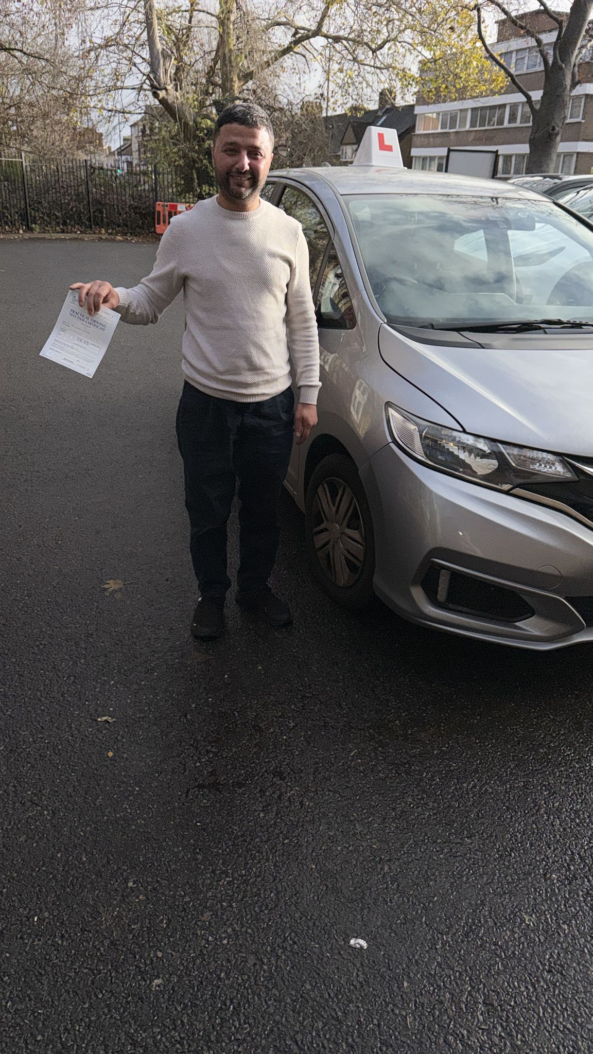 Passed student holding a driving test pass certificate beside a learner car
