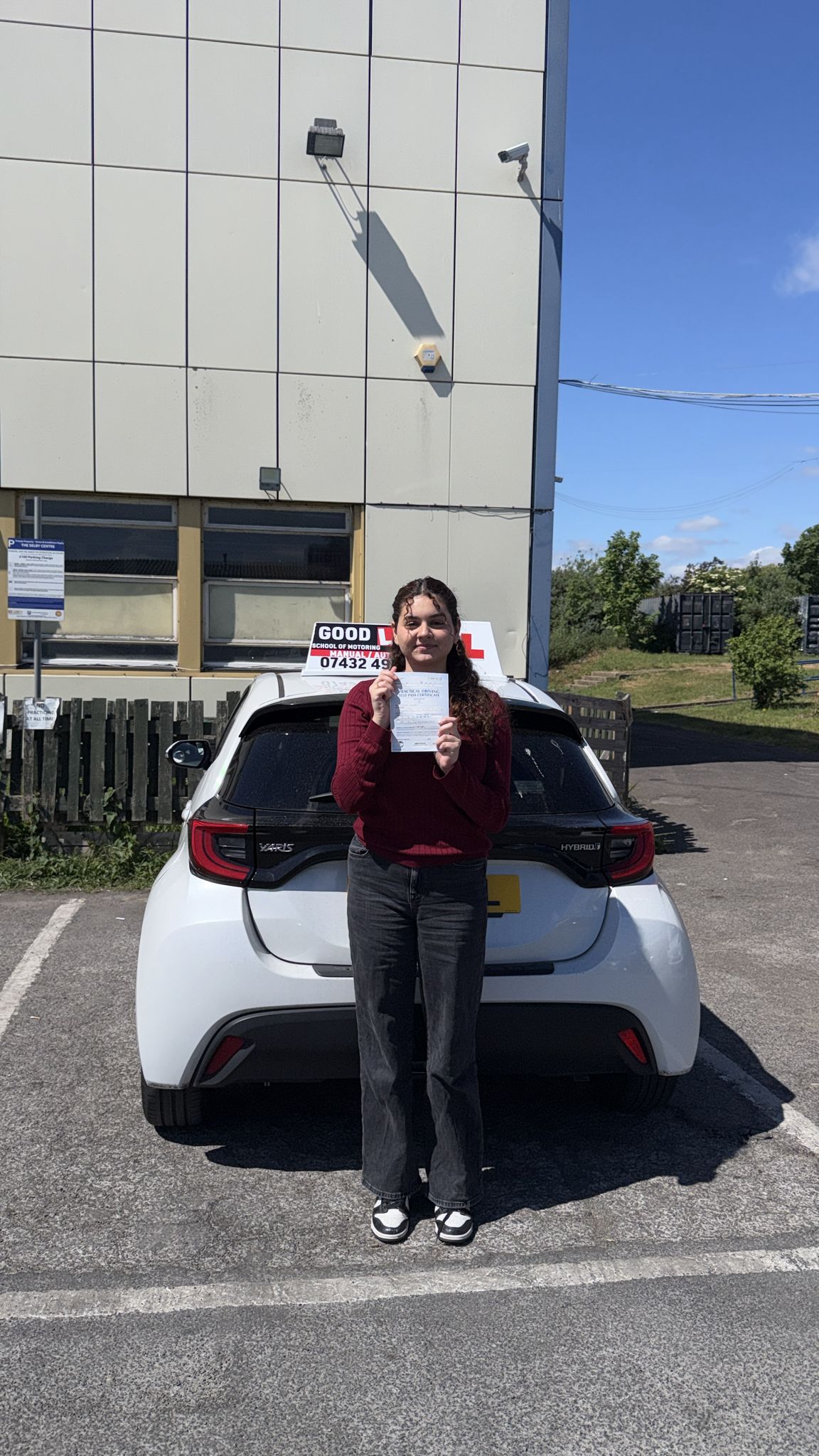 Passed student holding a driving test pass certificate beside a learner car