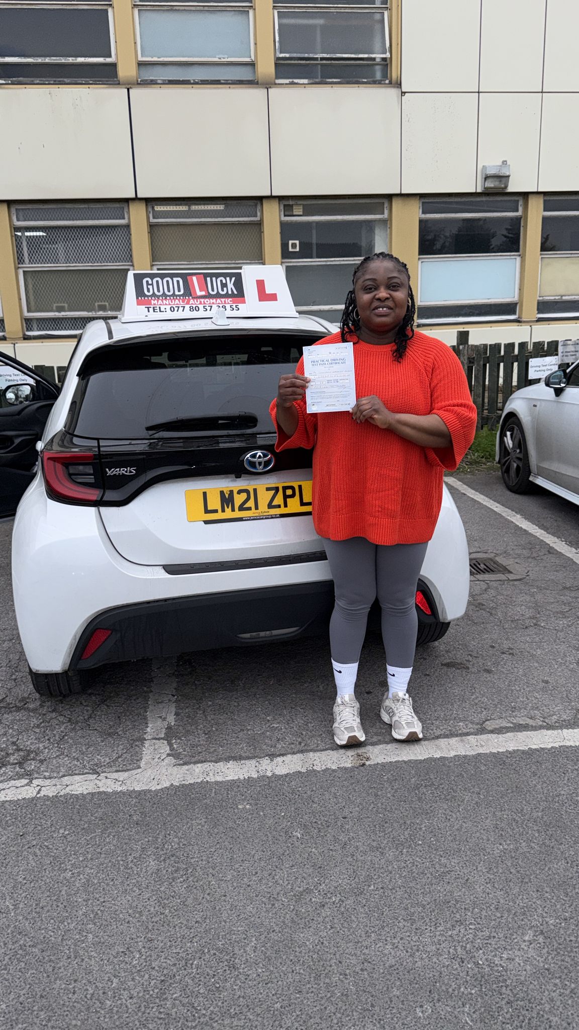 Passed student holding a driving test pass certificate beside a Good Luck learner car